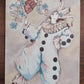 Pierrot I porte un costume bleu pâle et blanc surdimensionné, avec collerette, pompons noirs et petites chaussures rouges, œuvre originale d’Ana Jarén.