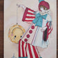 Pierrot III avance dans un costume rouge et bleu exagéré avec grand nœud turquoise et pompons rouges, œuvre originale d’Ana Jarén.