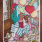 Une femme en pyjama rayé lit dans un fauteuil rose sous un grand bouquet de ballons pastel et en forme de cœur, œuvre originale d’Ana Jarén.