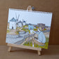 Une femme dessine les moulins de La Manche en plein paysage, feuille posée sur les genoux, œuvre originale d’Ana Jarén.
